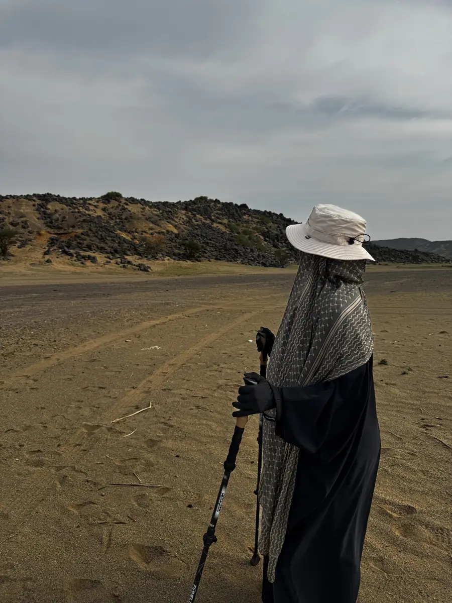 A sister in a sun hat and scarf looking across a wide sandy plain