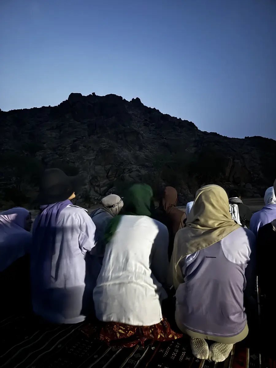 Sisters praying Fajr in rows before a dark mountain