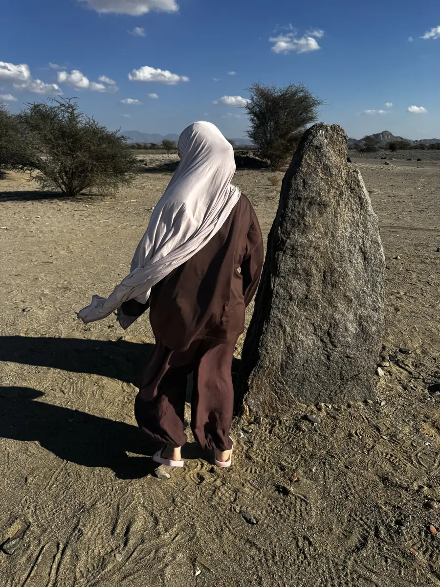 A sister resting a hand on a standing stone in the desert